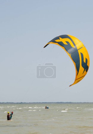 Photo for Henichesk, Ukraine - July 12, 2021: Surfer in wetsuit do trick. Kitesurfing athlete on kite board. Foiling kiteboarding kitesurfing kiteboarder in ocean. Kitesurfing. Seascape with surfer in waves. - Royalty Free Image