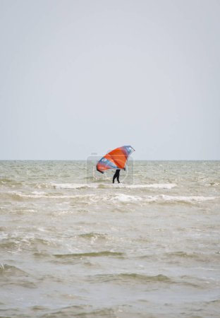 Photo for Henichesk, Ukraine - July 12, 2021: Surfer in wetsuit do trick. Kitesurfing athlete on kite board. Foiling kiteboarding kitesurfing kiteboarder in ocean. Kitesurfing. Seascape with surfer in waves. - Royalty Free Image