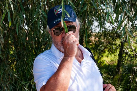 Hombre hispano anciano hombre mayor con elegante barba gris en estilo verano gorra cubana y gafas de sol al aire libre, divirtiéndose.