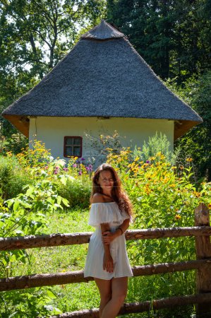 Woman in summer farm. Authentic Ukrainian architecture. Woman outdoor. Ukrainian woman in summer village cottage. Ukraine folk authentic house home. Thatched house in Ukrainian village.