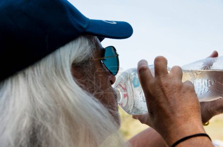 Senior thirsty man feel thirst and drinking water from sport bottle for healthy hydration balance. Drink water in summer heat.