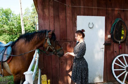 Woman with horse in stable at countryside ranch. Girl horse rider in summer outdoor. Equestrian and horseback riding. Horse stallion equine with Hispanic woman girl. Countryside ranch. Bridle and bit.