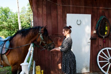 Woman with horse in stable at countryside ranch. Girl horse rider in summer outdoor. Equestrian and horseback riding. Horse stallion equine with Hispanic girl. Countryside ranch. Hooves pounding.