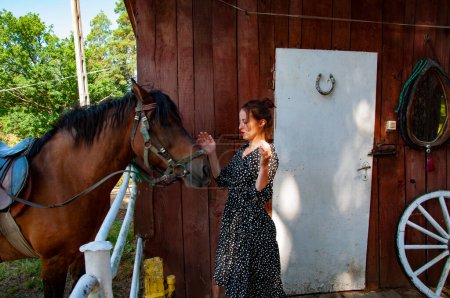 Photo for Woman with horse in stable at countryside ranch. Girl horse rider in summer outdoor. Equestrian and horseback riding. Horse stallion equine with Hispanic girl. Countryside ranch. Bridle and reins. - Royalty Free Image