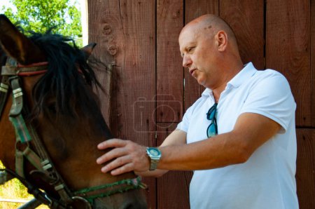 Man with horse in stable at countryside ranch. Man horse rider in summer outdoor. Equestrian and horseback riding. Horse stallion equine with Caucasian man. Countryside ranch. Take care.