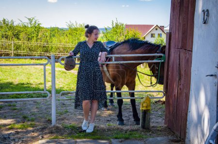 Woman with horse in stable at countryside ranch. Girl horse rider in summer outdoor. Equestrian and horseback riding. Horse stallion equine with Hispanic girl. Countryside ranch. Ranching economy.