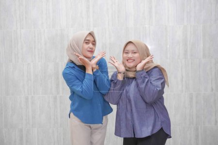 Two Asian Indonesian women wearing hijabs wearing light blue and dark blue clothes