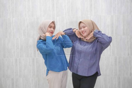 Two Asian Indonesian women wearing hijabs wearing light blue and dark blue clothes