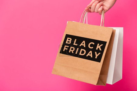 Black Friday, female hand holding two shopping bags isolated on pink background. Black friday sale, discount, shopping and ecology concept