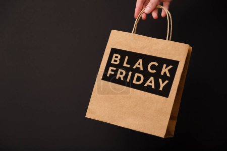 Black Friday, weibliche Hand hält Craft-Einkaufstasche isoliert auf schwarzem Hintergrund. Black Friday Sale, Discount, Recycling, Shopping und Umweltkonzept