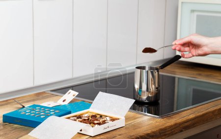 Téléchargez les photos : Zurich, Switzerland - January, 7 2023: Lindt Mini Pralines Box. Open small gift box of Swiss chocolate candies and hand of young woman making Turkish coffee at kitchen stove top. - en image libre de droit
