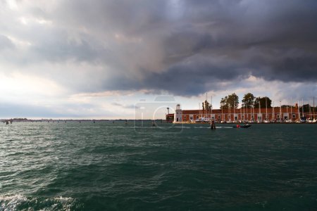 Venice, the lighthouse Faro of San Giorgio Maggiore island viewed from water, from sailboat with dark blue stormy sky in background.
