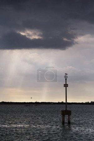 Waterway marker and uninhabited islands of Venetian lagoon with dark stormy sky in background. View from Burano island, Venice, Italy.