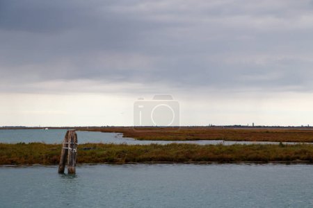 Old mooring post and uninhabited islands of Venetian lagoon. View from Burano island, Venice, Italy.
