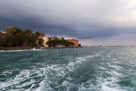 Venice vaporetto or water bus stop at Sacca Fisola island, Giudecca in Venetian Lagoon with dark blue stormy sky in background. Public transport route from cruise port in Venice, Italy.