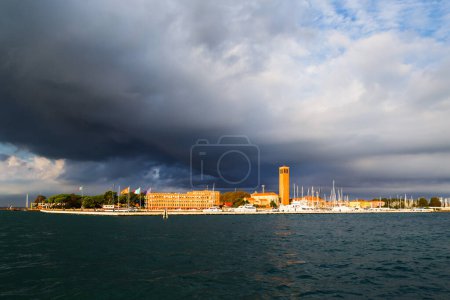 Bell tower of Sant'Elena Church and yacht harbor at extreme east end of sestiere of Castello in Venice, Italy. View from Venetian lagoon in stormy weather with dark cloudy sky in background.