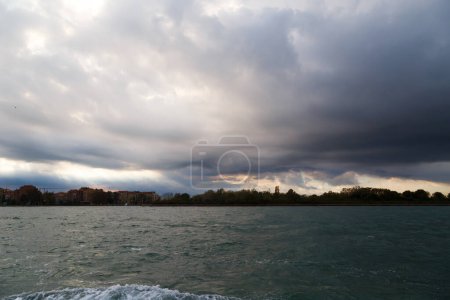 Venice, Italy. Giudecca and Sacca San Biagio islands in Venetian Lagoon with dark blue stormy sky in background. View from water bus