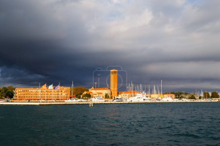Bell tower of Sant'Elena Church and yacht harbor at extreme east end of sestiere of Castello in Venice, Italy. View from Venetian lagoon in stormy weather with dark cloudy sky in background.