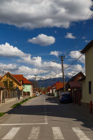 Typical street in Romanian town of Avrig leading to snowy Carpathian mountains, Romania. Bright sunny day.