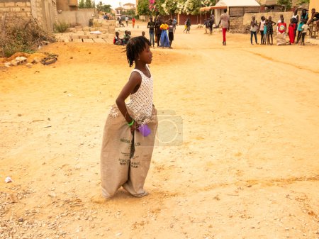 Photo for MBOUR, SENEGAL, AFRICA - DECEMBER Circa, 2021. Unidentified young african children doing a sack race in the street. They have to fill the basin with water to begin. Team sport very funny - Royalty Free Image