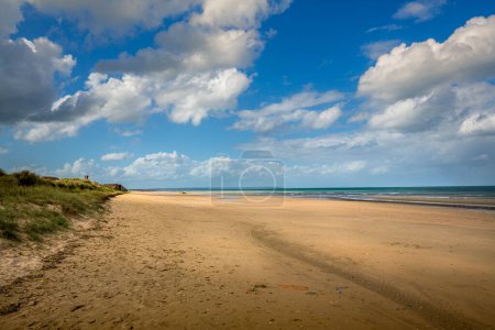 Téléchargez les photos : Vue large de la belle plage avec du sable doré et de l'eau bleue claire en arrière-plan sous un ciel nuageux bleu. - en image libre de droit