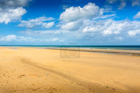 Téléchargez les photos : Vue large de la belle plage avec du sable doré et de l'eau bleue claire en arrière-plan sous un ciel nuageux bleu. - en image libre de droit