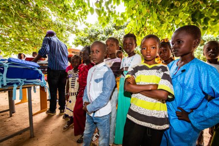 Photo for MBOUR, SENEGAL - DECEMBER Circa, 2020. Group of unidentified teenagers standing up in playground of the school , outdoors on a sunny summer day. Waiting for new bags given by international ngo. Sad and poor children. - Royalty Free Image