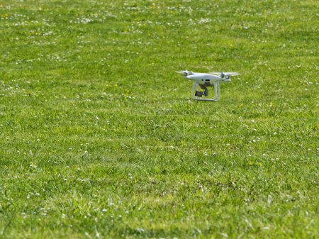 Photo for White quadrocopter flying under grass, close-up. New unmanned aerial copter. Electronics innovation.Aeromodelling. Modern Technologies. - Royalty Free Image