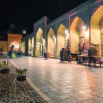 Lively night street sales in historic center of Bukhara with blurred people, carpet and souvenirs sellers.