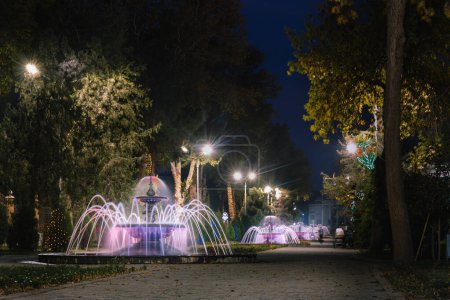 Photo for Park Kamal Khudzhandi alee with beautiful evening illumnation ,musical fountains and motion blurred people. . Khujand, Tajikistan. - Royalty Free Image