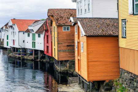 Traditional wooden buildings, painted in vibrant hues, line the river waterfront and create a picturesque and charming atmosphere. Sogndalstrand, Norway