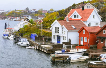 Sommerliche rot-weiße Hütten am Wasser, mit Booten, die an der Seebrücke anlegen, Sommerhütten am Meer auf der Insel Flekkeroya. Kristiansand, Norwegen