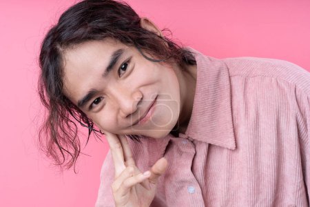 Foto de Joven asiático de pelo largo, con camisa rosa, sonriendo sobre fondo rosa - Imagen libre de derechos