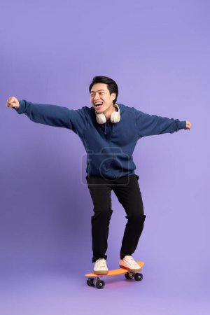 Image de jeune homme asiatique jouant skateboard sur fond violet