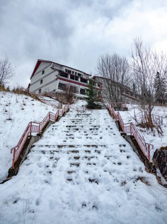 In winterlicher Berglandschaft führen verlassene Betontreppen zu einer trostlosen Villa in einem ehemaligen Ferienort inmitten der verschneiten Berglandschaft. Vidra, Karpathien, Rumänien.