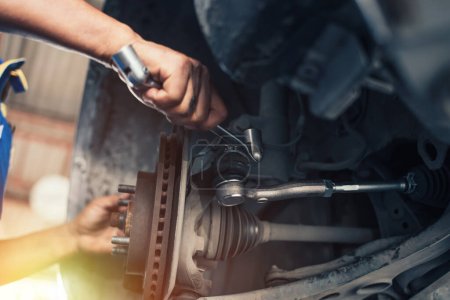 Téléchargez les photos : At a repair shop, a car mechanic tightens the suspension of an elevated vehicle with a spanner. - en image libre de droit
