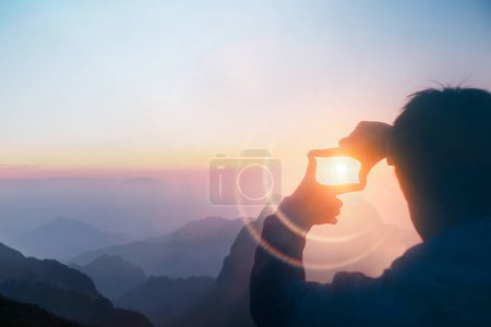 Photo for Silhouette of a person capturing sunlight in their hand during a beautiful mountain sunrise, creating a magical effect - Royalty Free Image