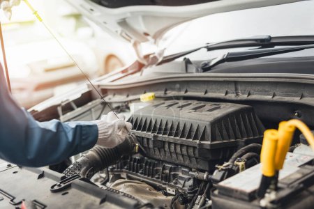 Auto technician inspecting under the hood of a vehicle, focusing on engine maintenance