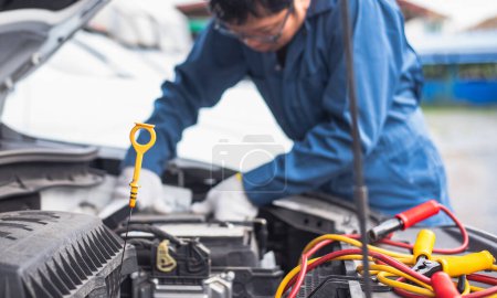 Automechaniker in blauer Uniform inspiziert Motoröl mit Messstab in einer Werkstatt