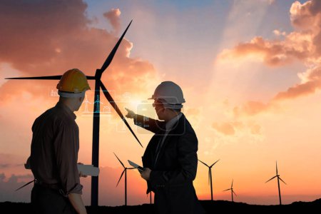 Photo for Two engineers with blueprints discussing wind turbines during a vibrant sunset in the background - Royalty Free Image