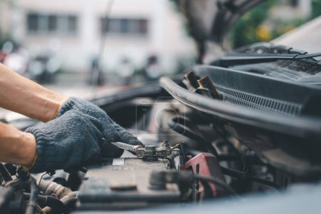 Skilled auto mechanic in gloves changing an expired car battery, focused on engine maintenance work