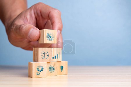 Hand placing the final wooden block with a target icon on a stack symbolizing business growth and goals