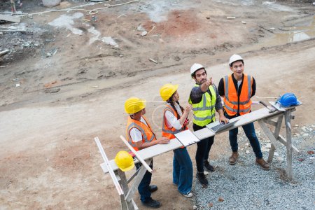 Un equipo de construcción diverso en equipo de seguridad discute planes sobre planos en un sitio de construcción