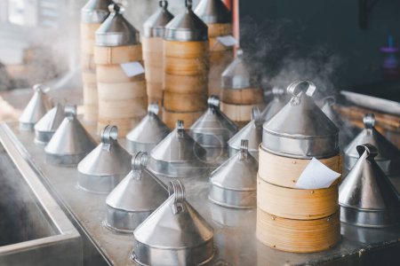 Dampfende Bambusdampfer türmen sich hoch in einer voll besetzten Küche und präsentieren den Kochprozess des traditionellen Dim Sum