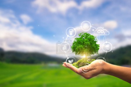 Eine Hand hält einen üppigen Baum mit Symbolen, die nachhaltige Energie und ökologische Konzepte vor einer malerischen Landschaft symbolisieren
