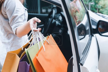 Foto de Primer plano de las manos de una mujer la colocación de bolsas de compras de colores en un coche blanco después de una juerga de compras - Imagen libre de derechos