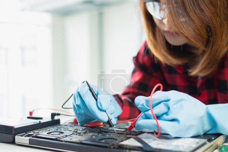 Konzentrierter Techniker mit Schutzbrille repariert ein elektronisches Laptop-Motherboard im Labor.