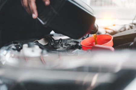 Primer plano de la mano de un mecánico vertiendo aceite de motor en el motor de un coche a través de un embudo durante el mantenimiento.