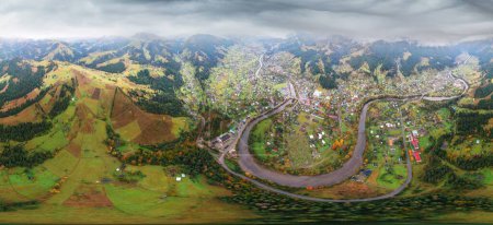 Aus der Vogelperspektive überfliegt eine Drohne im Herbst die Karpaten, das Bergdorf Werchowina in der Ukraine. Buchen- und Nadelwälder, Häuser, Straßen und ein Fluss im Tal