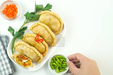 Téléchargez les photos : Pastels frits, en Indonésie connu sous le nom de Pastel goreng. Pâtisserie frite avec garniture de légumes, poulet et oeuf cuit servi avec du piment cru dans une assiette sur fond blanc à la main. Espace de copie de vue supérieure - en image libre de droit
